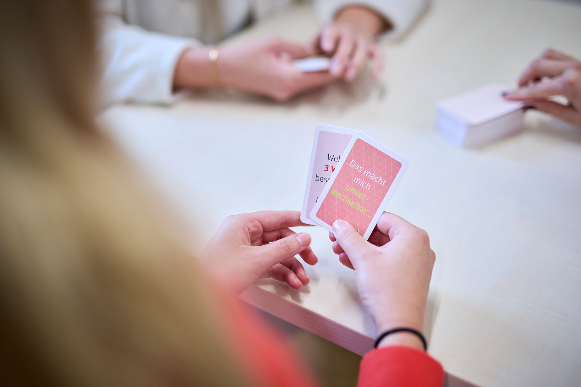Das Bild zeigt eine Therapiesituation. Ein Mädchen, das nur von hinten zu sehen ist, hält Gefühlskarten und bespricht diese mit der Therapeutin.