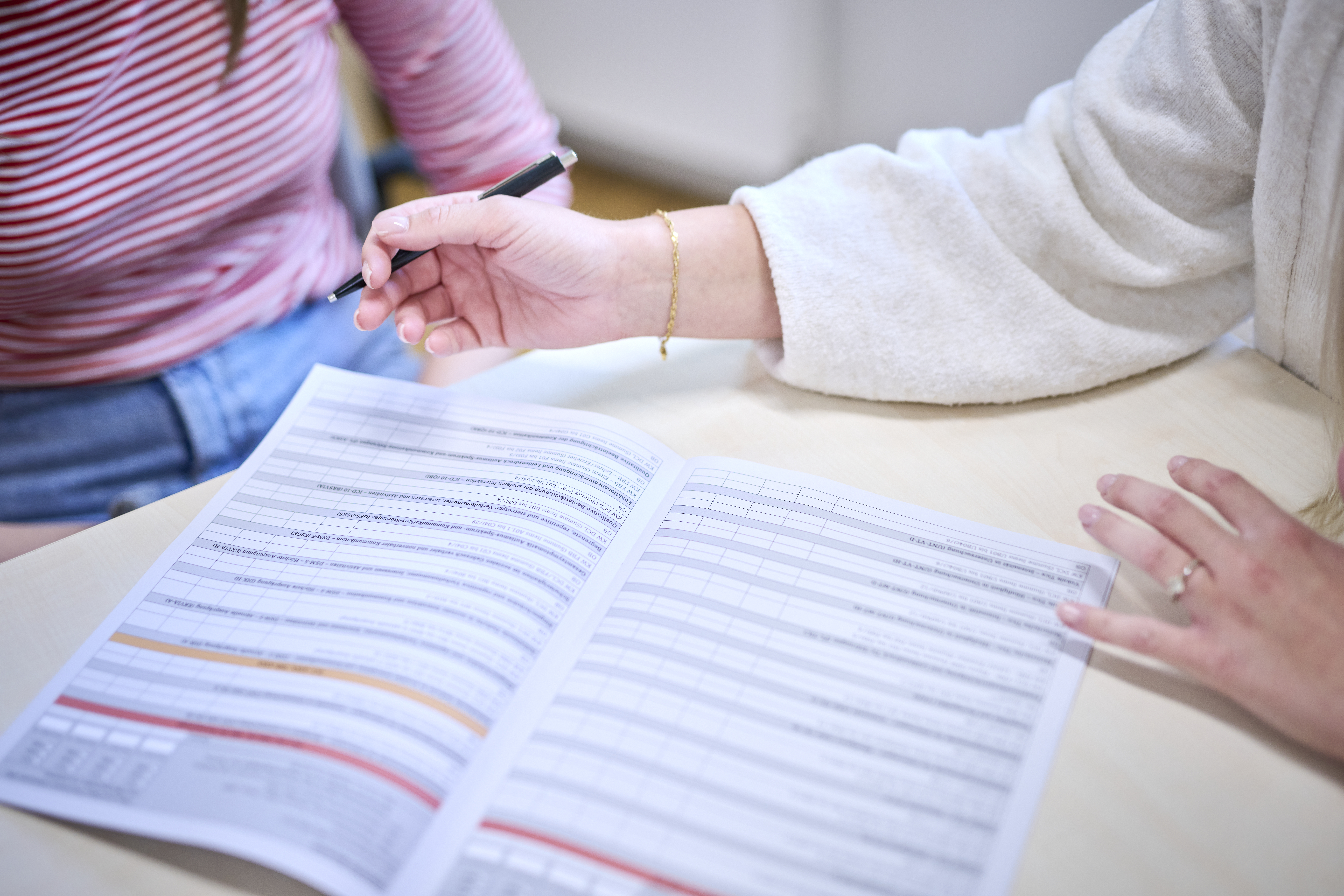 Eine Mitarbeiterin füllt im Beisein einer Patientin einen Diagnostikbogen aus.